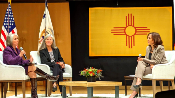 NM Gov Michelle Lujan Grisham, Dr. Eve Espey of UNM and Vice President Kamala Harris at UNM ABQ Visit Oct 2022 for Reproductive Justice, sitting on stage with NM state flag behind them.