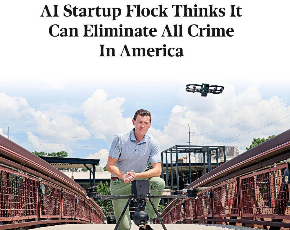 Screen capture image of a Forbes.com article. Flock Safety CEO Garrett Langley is on bended knee in front of a drone with cameras. They are framed by railings from a bridge he is on, and there are warehouse structures in the background. In black at the top the title says AI Startup Flock Thinks It Can Eliminate All Crime in America.