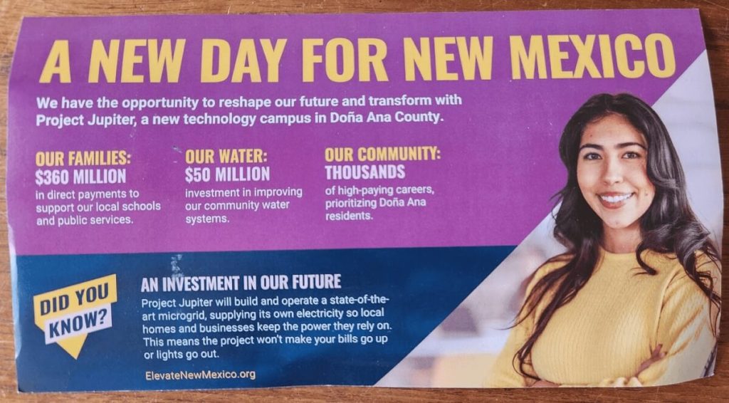 Photograph of a mailer. Gold text at top against purple background says A New Day For New Mexico. Below it is text in white that says: We have the opportunity to reshape our future and transform with Project Jupiter, a new technology campus in Doña Ana County. Our families: $360 million direct payments to support our local schools and public services. Our water: $50 million investment in improving our community water systems. Our community: thousands of high paying careers, prioritizing Doña Ana residents. 
